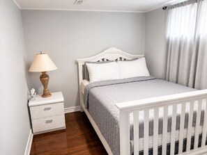 Une chambre à coucher avec un berceau blanc, une table de chevet avec une lampe et une commode.