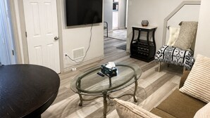 A living room with a glass coffee table, a flat-screen TV mounted on the wall, a sofa, and a patterned throw blanket. - Maple Haven | Spacious 3BR Private Luxury Suite • Huge Yard • Sleeps 6 (Pickering)