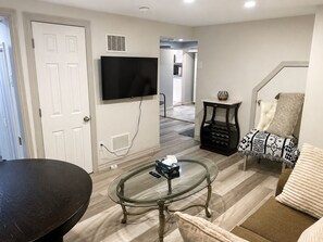 A living room with a glass coffee table, a flat-screen TV mounted on the wall, a sofa, and a patterned throw blanket. - Maple Haven | Spacious 3BR Private Luxury Suite • Huge Yard • Sleeps 6 (Pickering)