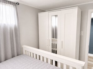 A bedroom with a white crib, a wardrobe, and a window with curtains. - Maple Haven | Spacious 3BR Private Luxury Suite • Huge Yard • Sleeps 6 (Pickering)
