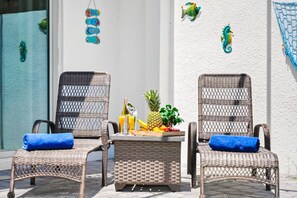 Zwei Korbstühle mit blauen Kissen und ein kleiner Tisch mit Früchten und Getränken.