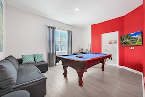 Quarto com mesa de bilhar, sofá e uma parede de destaque vermelha.