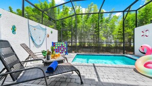 Área de piscina externa com estrutura de vidro, espreguiçadeiras, uma mesa com bebidas e um flutuador.