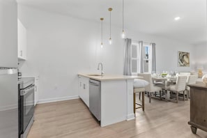 Uma cozinha moderna com uma ilha central, uma área de refeições com mesa e cadeiras, e piso de madeira.