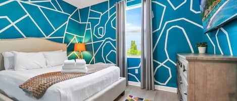 Una habitación de hotel con una cama, una mesita de noche, una lámpara, un aparador, una alfombra colorida y un ventanal con cortinas.