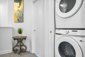 A laundry room with stacked washers and dryers, a small table with a plant, and a door with a white frame. - Heated Pool & Game Room Near Disney (Davenport)