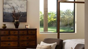 Une pièce dotée d’un ventilateur de plafond, d’une grande fenêtre donnant sur un paysage verdoyant, d’une commode en bois et d’un fauteuil en cuir marron.