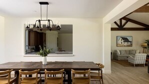 Un coin repas comprenant une grande table en bois, six chaises, un vase avec des plantes et un luminaire suspendu.
