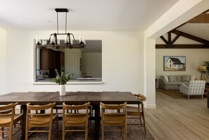 A dining area with a large wooden table, six chairs, a vase with greenery, and a pendant light fixture.