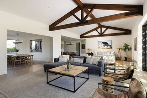 A spacious living area with a high ceiling and exposed beams, a dining area with a wooden table and chairs, and a cozy seating arrangement with a sofa and armchairs.