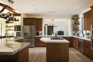 A modern kitchen with a central island, stainless steel appliances, wooden cabinets, and a large window providing natural light. - Desert Ranch Retreat, Luxury Stay, Weddings & Special Events (Indio)