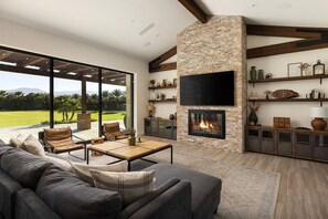 A modern living room with a fireplace, a large sofa, and a television mounted on a stone wall.