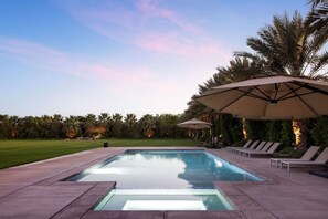 A swimming pool with lounge chairs and umbrellas, surrounded by palm trees and a well-maintained lawn.