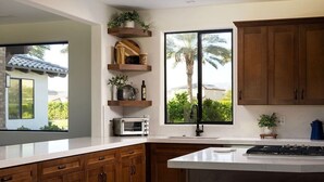 Une cuisine moderne avec des meubles en bois, un four à micro-ondes encastré et une grande fenêtre donnant sur des palmiers.