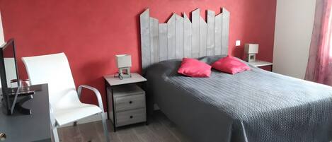 Ein Schlafzimmer mit einem Bett, einem Schreibtisch, einem Sessel, einem Nachttisch und einem Wandbild.