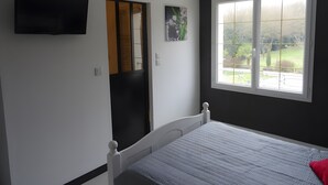 Um quarto com cama, televisão fixada na parede, janela com vista para o exterior e porta com espelho.