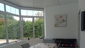 Uma área de refeições com uma mesa coberta por uma toalha florida, rodeada por cadeiras e um banco com almofadas vermelhas.