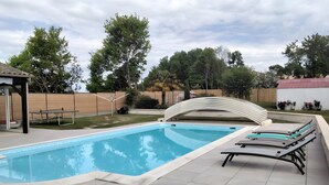 Piscina retangular com deck ladrilhado, rodeada por um espaço coberto com espreguiçadeiras.