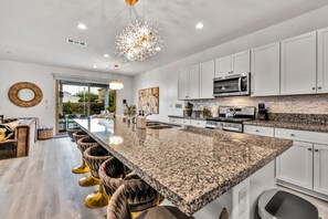 A modern kitchen with a large island, white cabinetry, and stainless steel appliances.