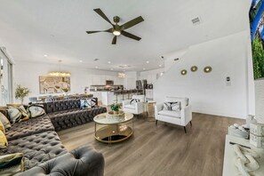 A modern living room with a sofa, armchairs, a coffee table, and a ceiling fan.