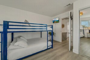 A bunk bed room with a television on the wall, a small plant, and a door leading to another room.