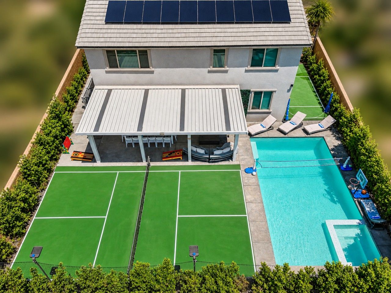 A modern house with a swimming pool, tennis court, and solar panels.