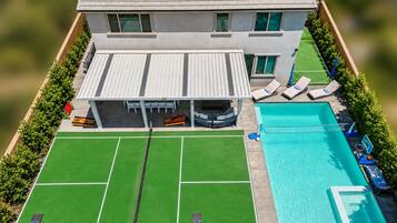 A modern house with a swimming pool, tennis court, and solar panels.
