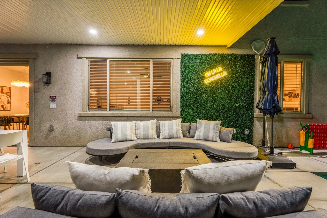 A modern living room with a curved sofa, a green wall, and a neon sign.