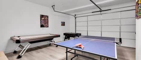 Una habitación con mesa de ping pong, mesa de fútbolín y mesa de billar.