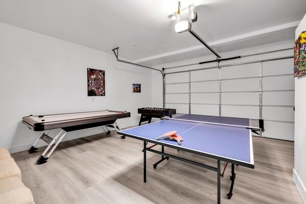 A room with a ping pong table, foosball table, and a billiards table.
