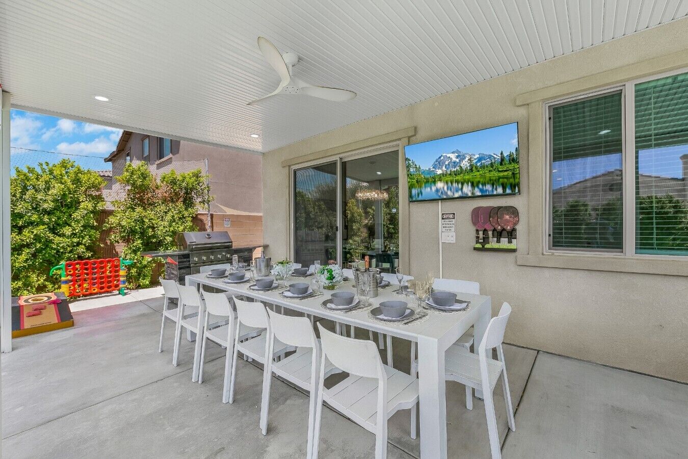 An outdoor patio with a dining table set for six, surrounded by white chairs.