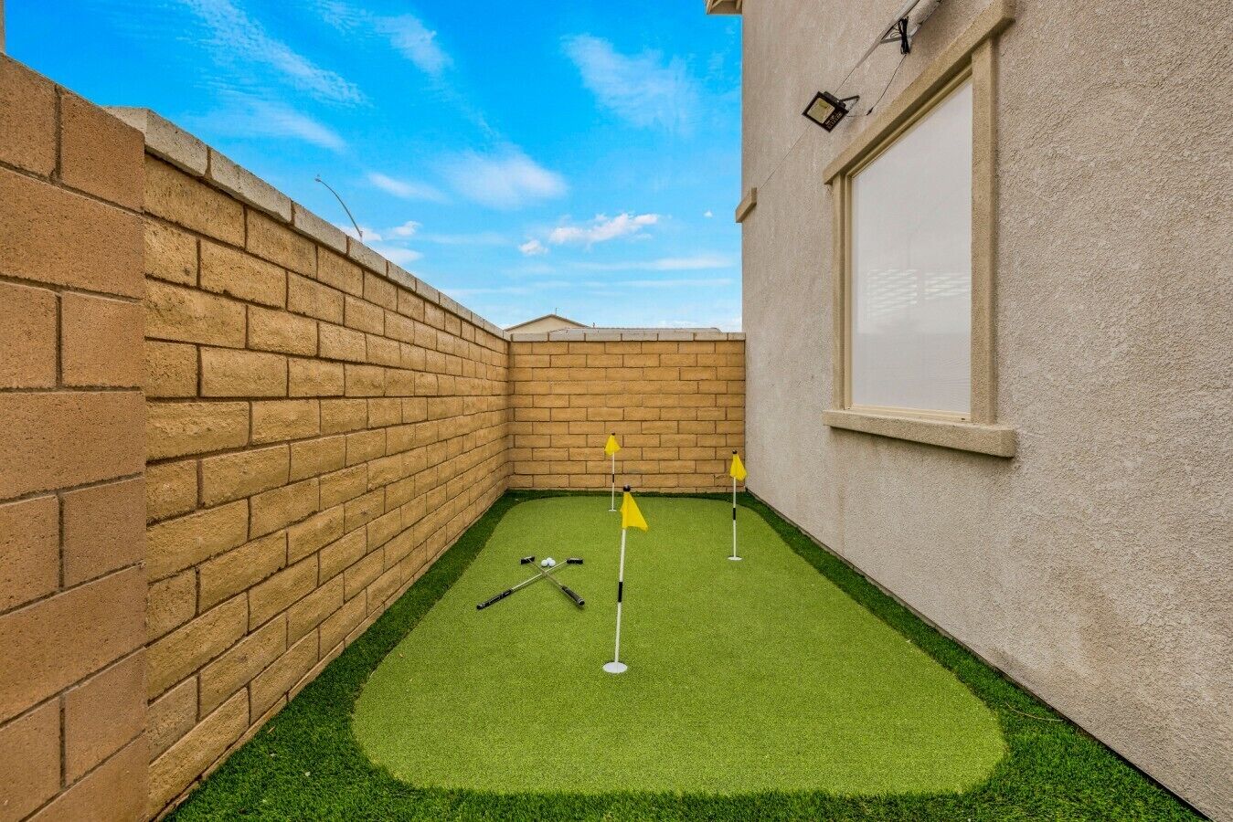 A small, enclosed space with artificial turf, a brick wall, and a window.