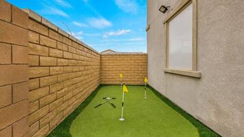 A small, enclosed space with artificial turf, a brick wall, and a window.
