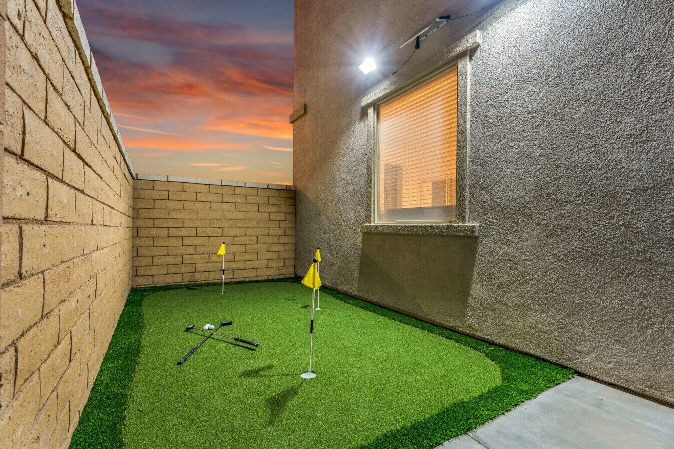 A small, enclosed space with artificial turf, a golf putting area, and a brick wall.