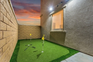 A small, enclosed space with artificial turf, a golf putting area, and a brick wall. - 8BR Luxury Pool Spa Pickleball Hoops Game Room BBQ - Sleeps 28 (Coachella)