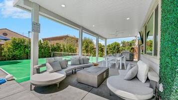 An outdoor patio with a covered seating area, a barbecue grill, and a tennis court visible in the background.