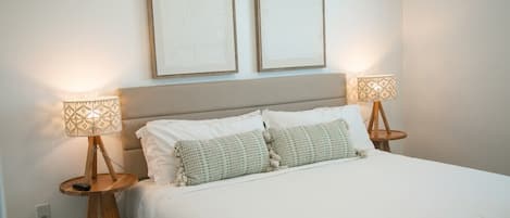 A bed with white bedding, two bedside lamps, and two framed artworks on the wall.