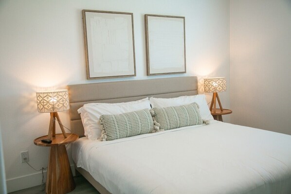 A bed with white bedding, two bedside lamps, and two framed artworks on the wall.