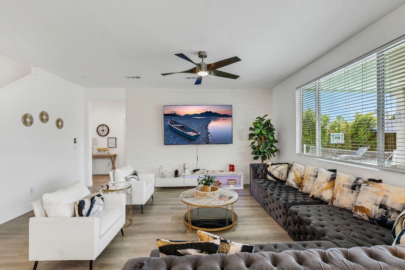 A modern living room with a white sofa, a dark tufted sofa, a round coffee table, and a television mounted on the wall.