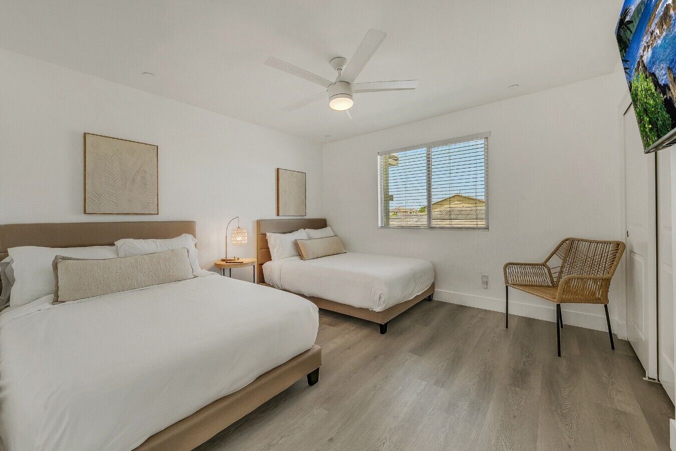 A hotel room with two beds, a ceiling fan, a window with a view, and a wicker chair.