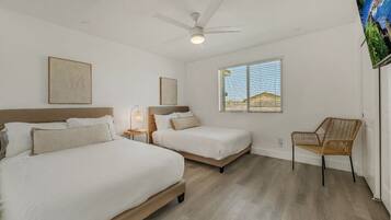 A hotel room with two beds, a ceiling fan, a window with a view, and a wicker chair.