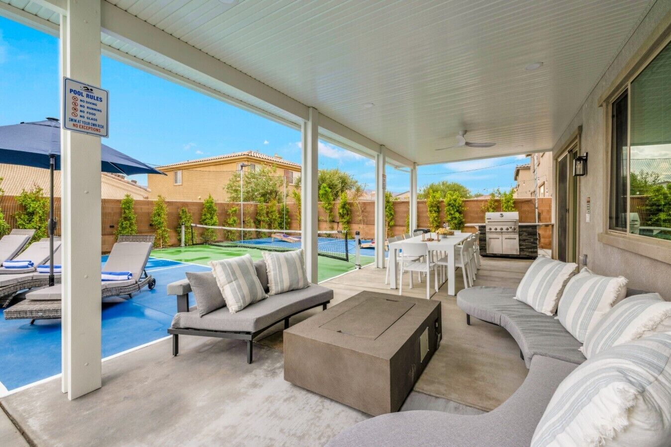 A covered outdoor area with a pool, lounge chairs, a dining table, and a barbecue grill.