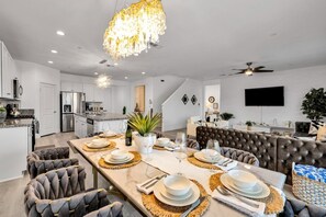 A modern kitchen with stainless steel appliances, a dining area with a marble table, and a living room with a large TV.