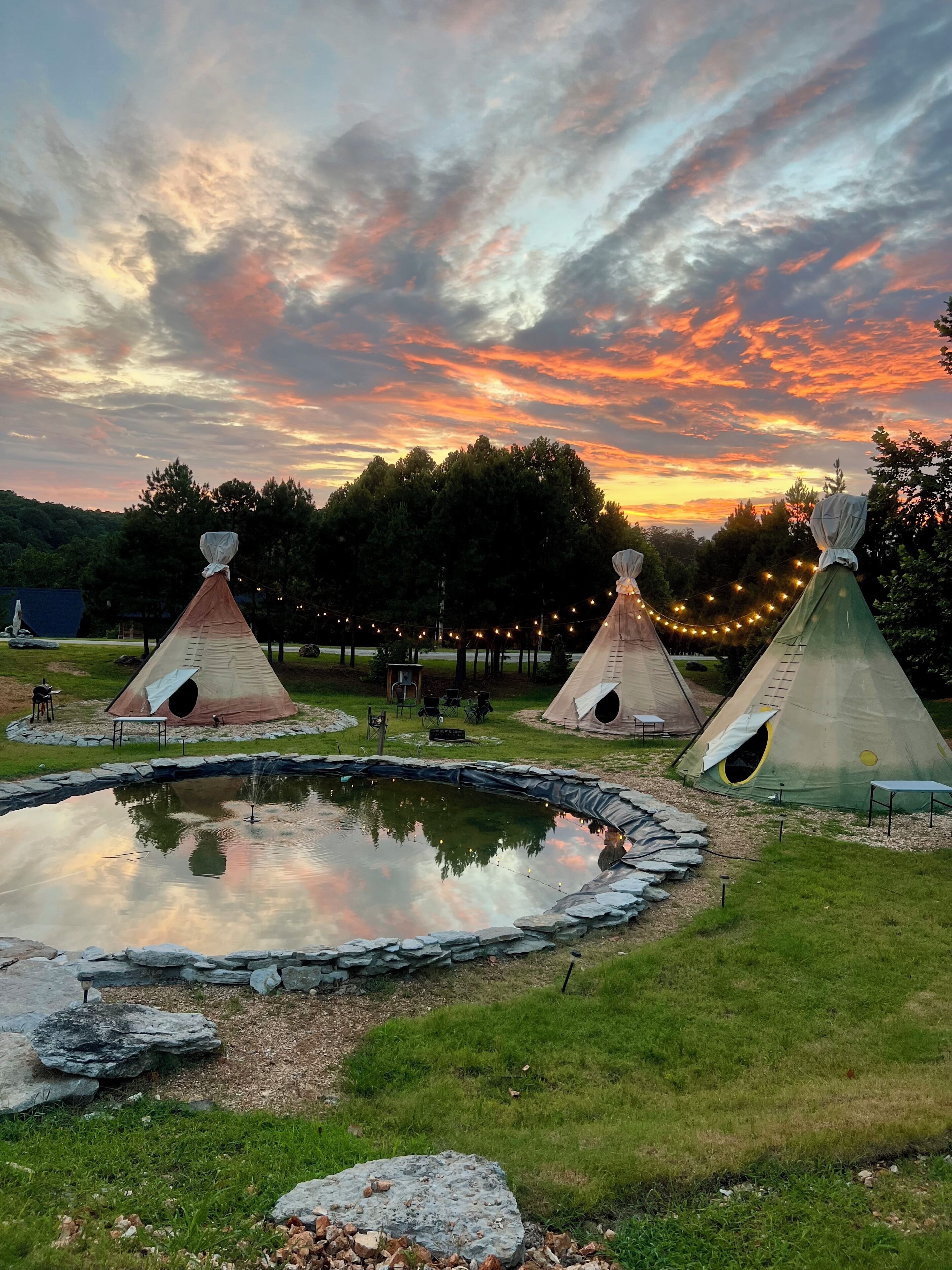 A campsite with teepees, a pond, and a sunset sky.
