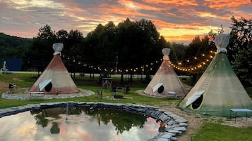 A campsite with teepees, a pond, and a sunset sky.