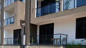 A multi-story building with balconies, large windows, and a paved ground area.