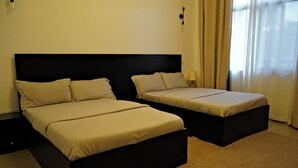 A hotel room with two beds, a black headboard, a lamp, and a window with curtains.