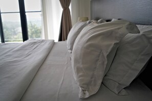 A bed with white linens and a headboard, a window with curtains, and a view of the outdoors.
