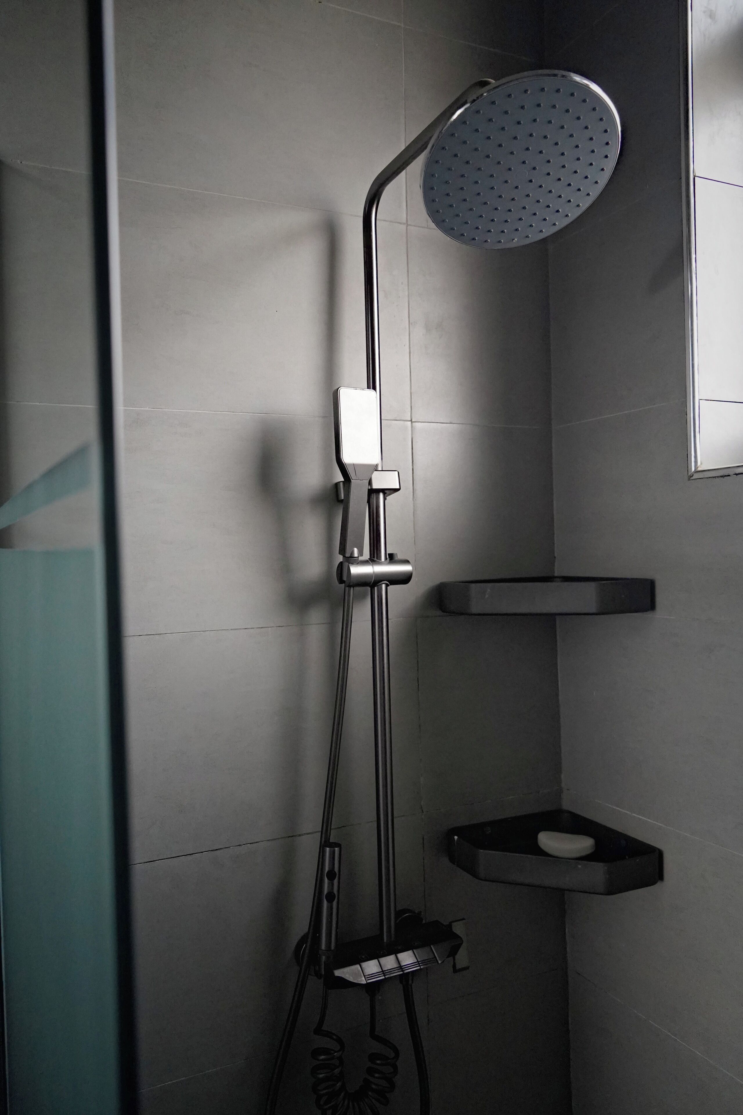 Eine moderne Dusche mit Duschbrause, Bedienfeld an der Wand und einer kleinen Ablage mit Seifenschale.