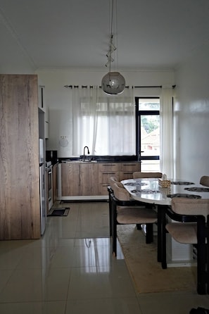 A modern kitchen with a central island, a dining table with chairs, and a large window with curtains.